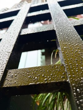 Detailed close up of crystal clear raindrops on textured dark olive metal fence after rain, dramatic urban abstraction