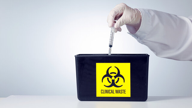 Professional hand drops syringe into biohazard bin, demonstrating proper clinical waste management with focused, responsible attitude