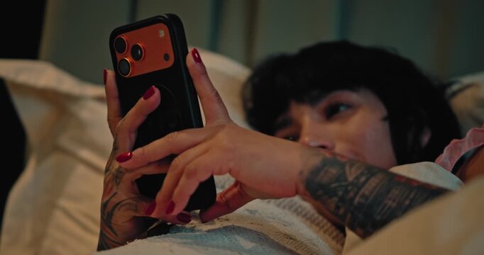 Close-Up of Tattooed Hands Using a Smartphone in Bed