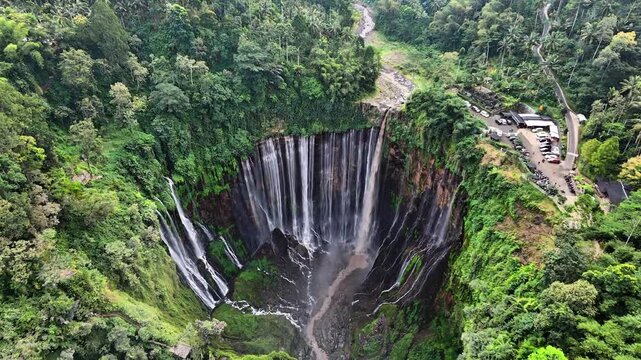 Aerial drone view of Tumpak Sewu Waterfall surrounded by lush green tropical forest in East Java, Indonesia