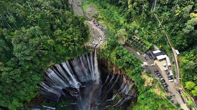 Aerial drone view of Tumpak Sewu Waterfall surrounded by lush green tropical forest in East Java, Indonesia