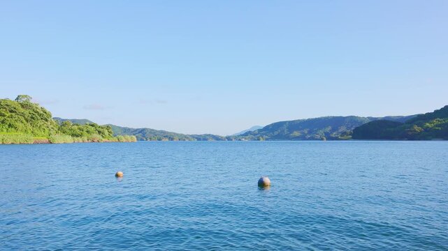 快晴の空と静かな青い海、山並みに囲まれた穏やかな湾の風景