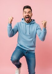 Fototapeta premium Excited Young Man Celebrating Success with Raised Fists and Shouting Joyfully on Pink Background