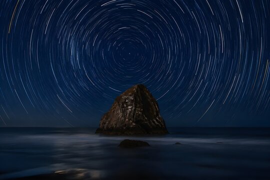 Concentric Star Trails Circle Above a Steadfast Sea Stack in the Dark Midnight Ocean Below