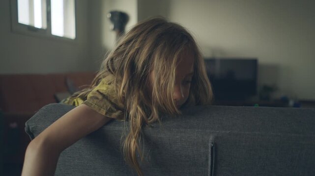 Child leaning over a couch armrest gazing downward