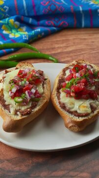 Toasted bread topped with layers of cheese, beans and pico de gallo salsa