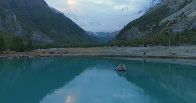 Annapurna Circuit, Manang, Humde Nepal, aerial drone pull out shot of the turquoise waters of Blue Lake reflecting alpine forests and misty mountains