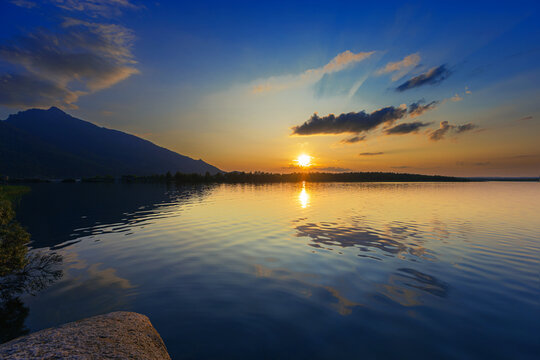 Golden sunset over Borovoe lake in Kazakhstan, path of light reflects on calm rippling water, orange and blue colored sky glows. Burabay National Nature Park Travel destination. Serene and peaceful.