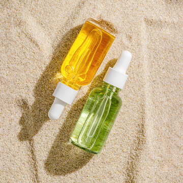 Natural facial skin care product in two glass bottles with white lid and pipette with liquid essence, serum on beige sand background. Eco beauty concept of cosmetic with organic botanical extracts.