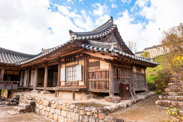 Obraz premium Panoramic View of Traditional Korean Hanok House Featuring Curved Tiled Roofs and Wooden Structure Under Autumn Sky