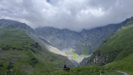 Dramatic mountain valley with green slopes and rocky cliffs under low clouds © 123sasha
