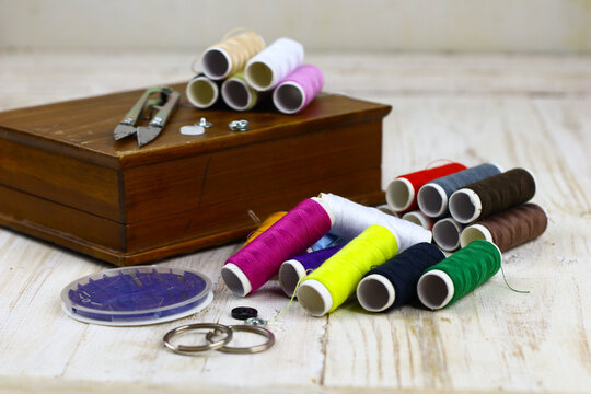 Colorful sewing thread spools with sewing accessories arranged on a rustic wooden table.