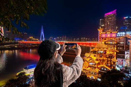 Female tourist photographing the stunning illuminated Hongyadong building complex at night in Chongqing, China