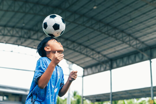 Young boy juggling soccer ball with foot at indoor field.