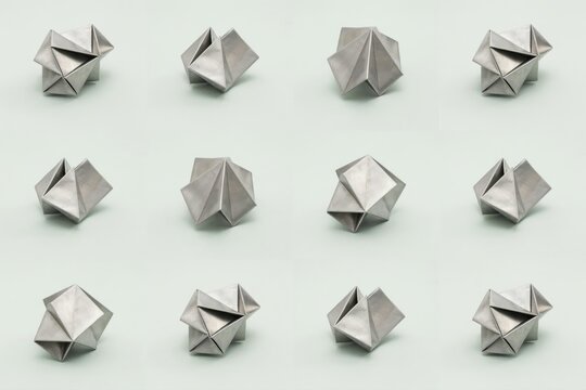 A collection of small silver metallic origami sculptures arranged in a grid on a light gray background, with sharp geometric folds