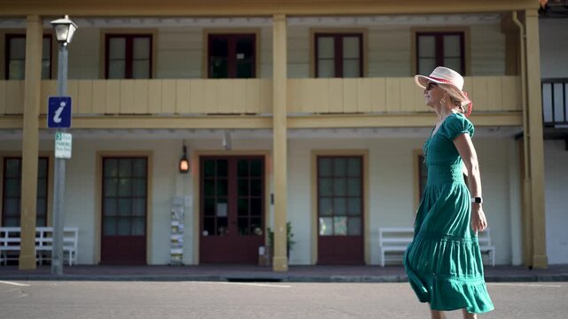 A smiling senior woman strolls alongside the historic Sonoma Barracks and Toscano Hotel in Sonoma, California during a sunny morning.