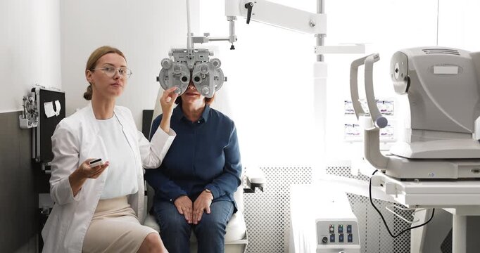 Medical vision specialist conducting eye examination of middle aged female patient with digital diagnostic tools performing phoropter eyesight test on appointment in modern clinic office. Copy space