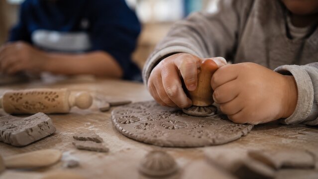 Close-up of Child's Hands Stamping Patterns into Gray Clay During a Creative Pottery Workshop for Early Childhood Education and Artistic Development