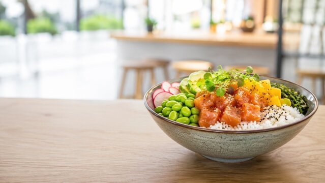 Fresh poke bowl on wooden table in bright cafe