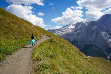 Fototapeta premium Young athletic woman hiking along an alpine trail with Marmolada and the Dolomites under a clear blue sky, South Tyrol, Italy