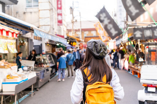 Young female tourist walking along busy food stalls, enjoying street food tour at Tsukiji Outer Market in Tokyo, Japan