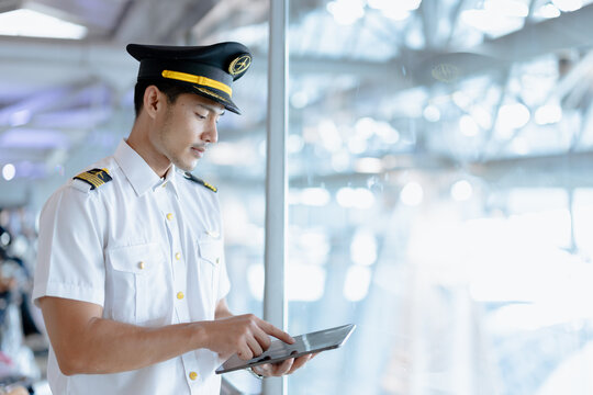 Asian steward or pilot man. Airline Airport service in uniform standing looking at tablet in airport background with copy space for text