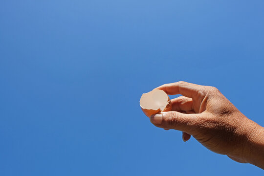 Hand holding an empty cracked eggshell against a clear blue sky. Minimal natural scene with copy space for sustainability, recycling, and food concepts