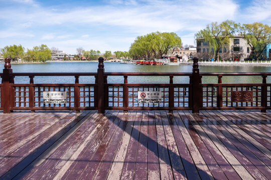 Wooden lakeside deck and railing overlooking willow-lined spring lake in Beijing park