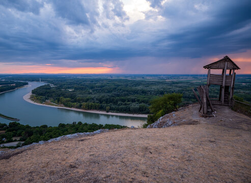 Celtic wooden lookout on Braunsberg Hill overlooking the Danube River and Donau-Auen floodplain beneath dramatic storm clouds at sunset near Hainburg an der Donau, Austria.