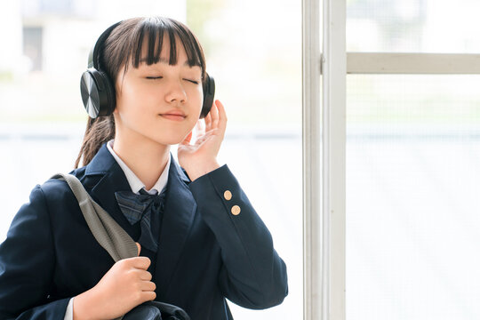 Elementary, middle, and high school girls in school uniforms listening to music with headphones in the school hallway.