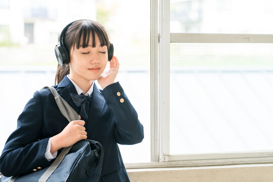 Elementary, middle, and high school girls in school uniforms listening to music with headphones in the school hallway.