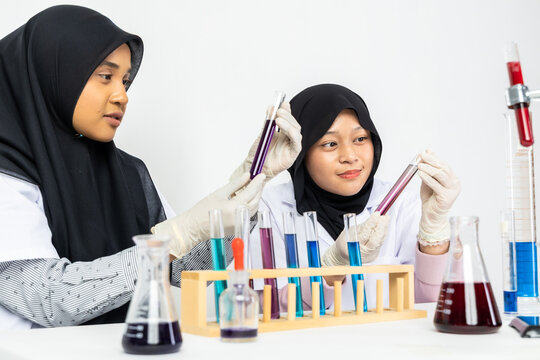 Two Muslim female scientists wearing hijab working in a chemistry laboratory with glassware and chemical solutions. Perfect for STEM education, research, science, healthcare, and biotechnology concept