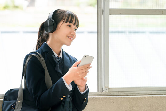 Elementary, middle, and high school girls in school uniforms listening to music with headphones in the school hallway.