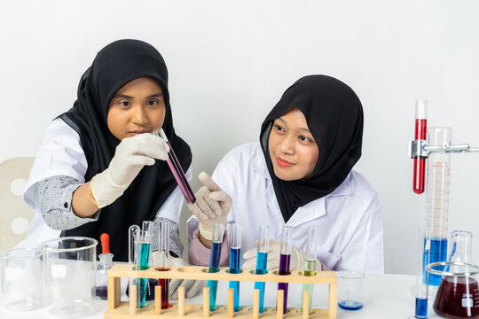 Two Muslim female scientists wearing hijab working in a chemistry laboratory with glassware and chemical solutions. Perfect for STEM education, research, science, healthcare, and biotechnology concept