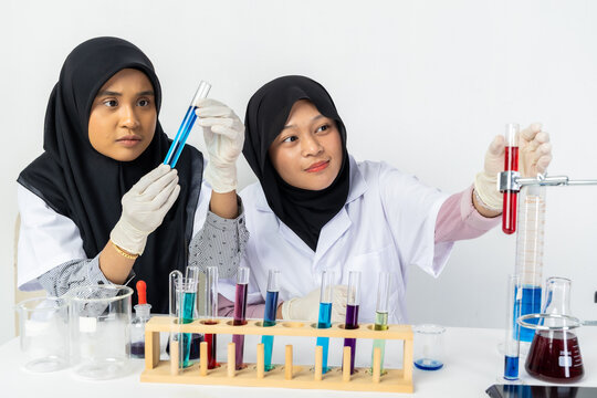 Two Muslim female scientists wearing hijab working in a chemistry laboratory with glassware and chemical solutions. Perfect for STEM education, research, science, healthcare, and biotechnology concept