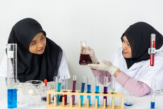 Two Muslim female scientists wearing hijab working in a chemistry laboratory with glassware and chemical solutions. Perfect for STEM education, research, science, healthcare, and biotechnology concept
