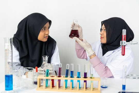 Two Muslim female scientists wearing hijab working in a chemistry laboratory with glassware and chemical solutions. Perfect for STEM education, research, science, healthcare, and biotechnology concept