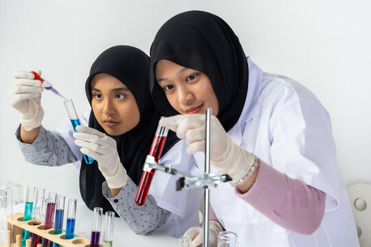 Two Muslim female scientists wearing hijab working in a chemistry laboratory with glassware and chemical solutions. Perfect for STEM education, research, science, healthcare, and biotechnology concept