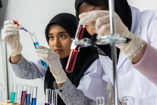 Two Muslim female scientists wearing hijab working in a chemistry laboratory with glassware and chemical solutions. Perfect for STEM education, research, science, healthcare, and biotechnology concept