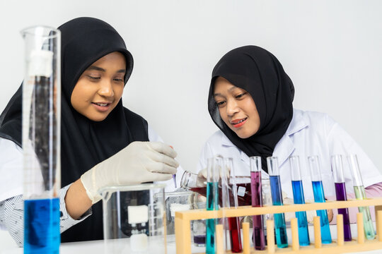 Two Muslim female scientists wearing hijab working in a chemistry laboratory with glassware and chemical solutions. Perfect for STEM education, research, science, healthcare, and biotechnology concept