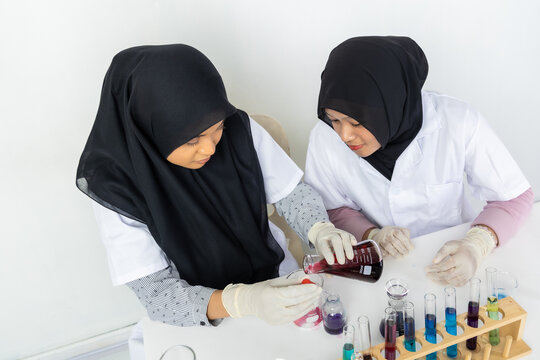 Two Muslim female scientists wearing hijab working in a chemistry laboratory with glassware and chemical solutions. Perfect for STEM education, research, science, healthcare, and biotechnology concept