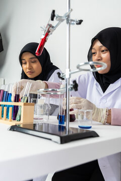 Two Muslim female scientists wearing hijab working in a chemistry laboratory with glassware and chemical solutions. Perfect for STEM education, research, science, healthcare, and biotechnology concept