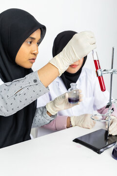 Two Muslim female scientists wearing hijab working in a chemistry laboratory with glassware and chemical solutions. Perfect for STEM education, research, science, healthcare, and biotechnology concept