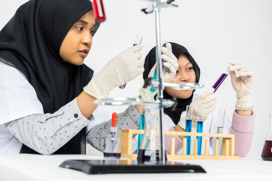 Two Muslim female scientists wearing hijab working in a chemistry laboratory with glassware and chemical solutions. Perfect for STEM education, research, science, healthcare, and biotechnology concept