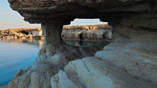 Drone view from inside the Cape Cavo Greco Sea Caves in Cyprus. Natural rock archways and the calm blue sea create a dramatic coastal scene.