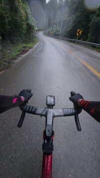 Vertical POV footage of a cyclist riding on a wet mountain road after rain through tropical forest, featuring reflective asphalt, gentle curves and a cinematic outdoor adventure.