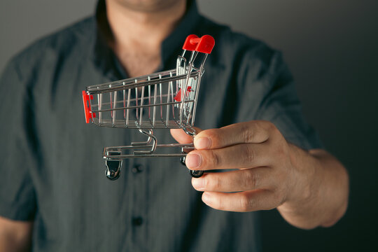 Male hand holding red shopping basket on grey background.