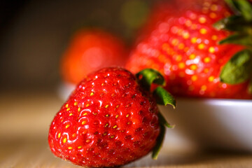 Side Macro of Fresh Red Strawberry with Warm Bokeh Bowl in Background on Wooden Table © Екатерина Переславце
