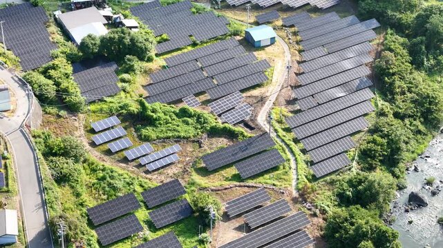 Rows of solar panels stretch across green hillsides. Winding road cuts through the installation. River flows beside the panels. No people appear in this scene. Ideal for clean energy, sustainability