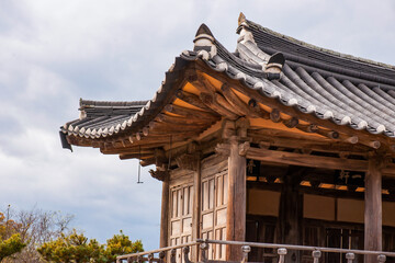 Obraz premium Detailed Close-Up View of Traditional Korean Hanok Curved Tiled Roof, Eaves, and Wooden Structure Against Cloudy Sky
